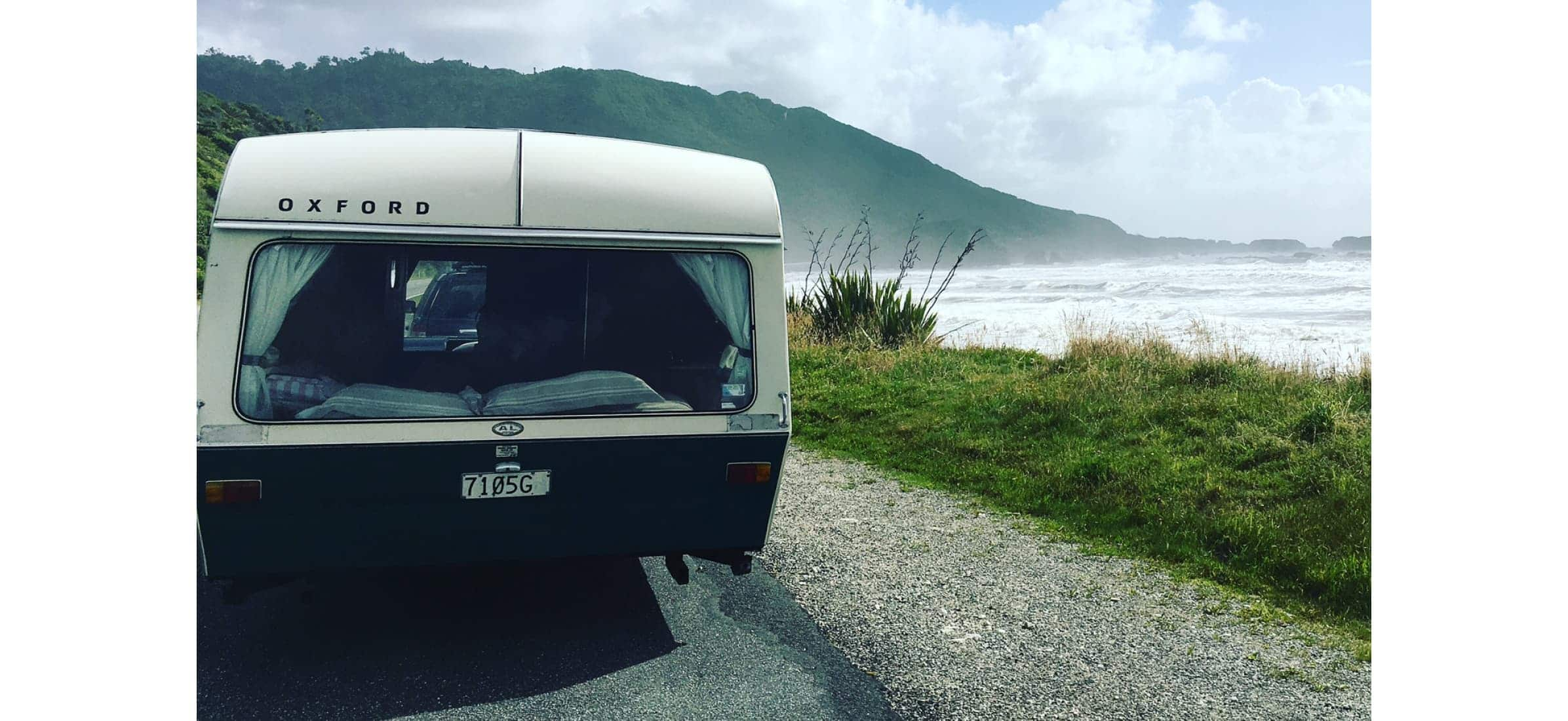 The back of a caravan sitting on the side of a road next to a beach.